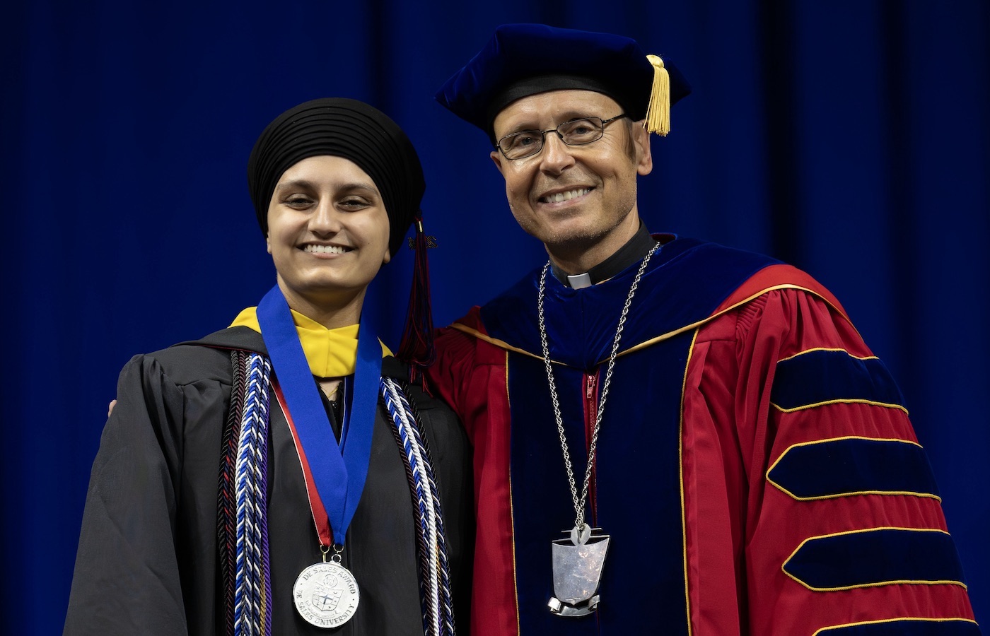 Harkiran Bhullar and Father James Greenfield on stage at Commencement