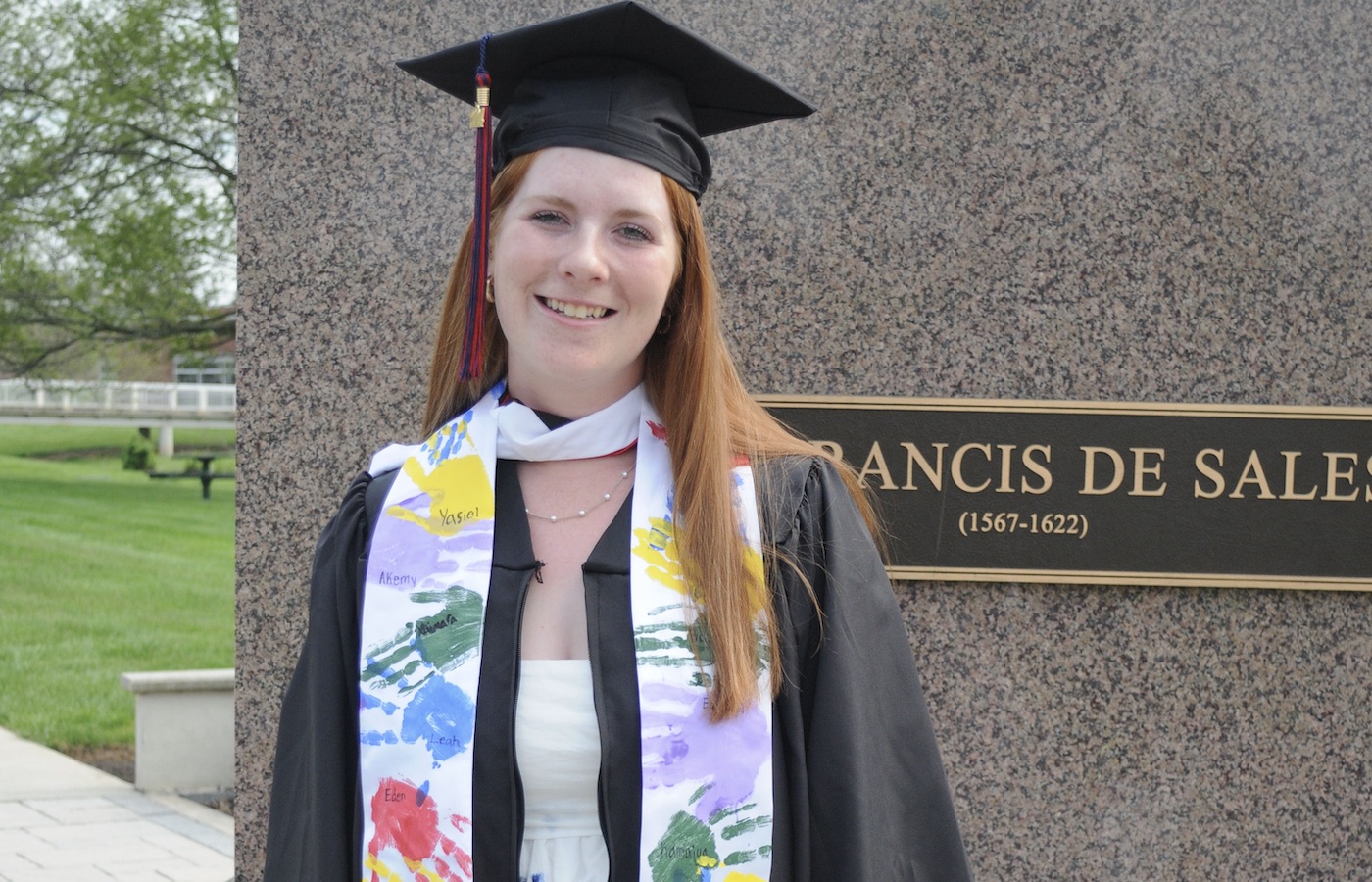 Morgan Landau in cap and gown by St. Francis statue